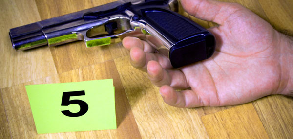 The hand of an apparently uncouncious person lying next to a firearm with a crime scene marker numbered five