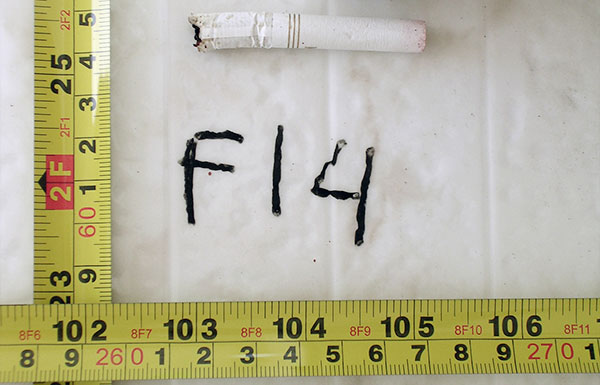 An evidence photo of a ciggarette on the floor, framed by measuring tapes.