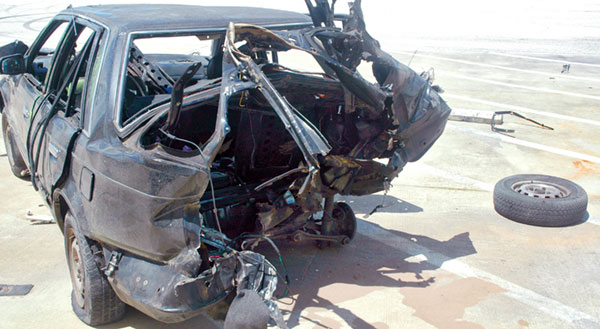 Photograph of a black car, burned and warped from an explosion iside the vehicle.