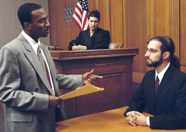 An attorney holding a paper file, questioning an expert witness on the stand in a court of law while the judge looks on. For illustration only.