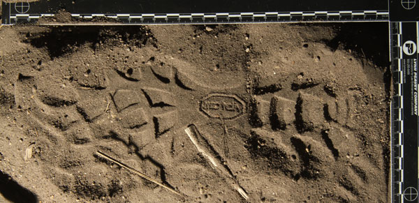 a three-dimensional shoeprint in soft sand framed with an L ruler