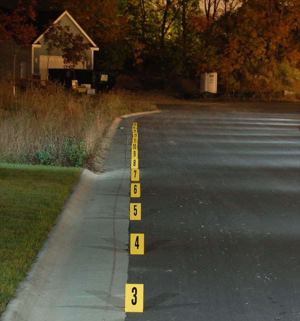 the same view of the evidence markers at night, but additional light has been added to see the detail including a building and plants