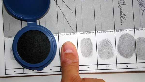 A person places their thumbprint on a document with their signature to affirm their identity